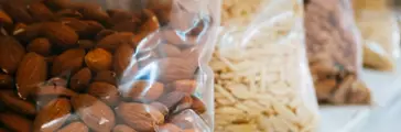 Plastic bag of almonds on a shelf with other bags of nuts.