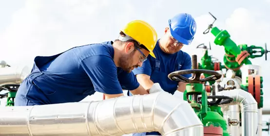 Two petrochemical workers inspecting pressure valves on a fuel tank
