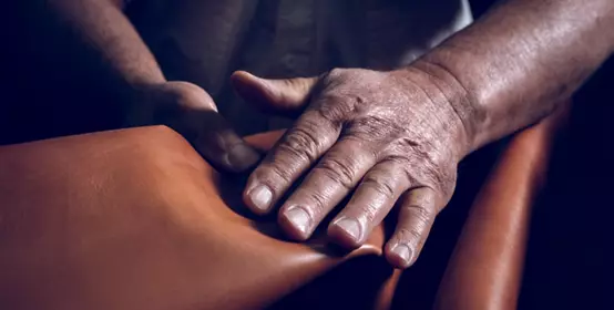 Crop craftsman laying leather on table, only hands visible.