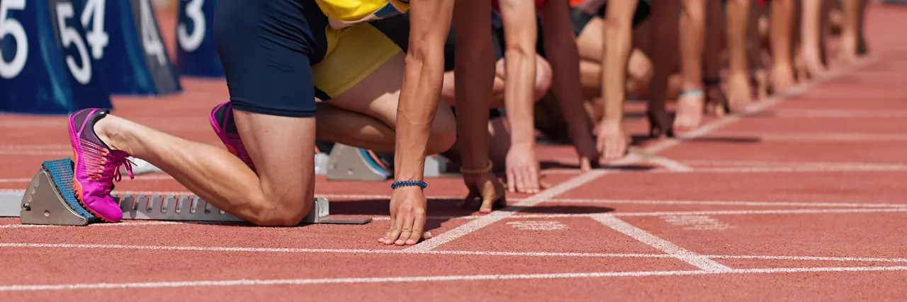 Group of male track athletes on starting blocks. Hands on the starting line. Athletes at the sprint start line in track and field