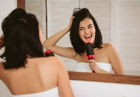 Young woman brushing healthy hair in front of a mirror 