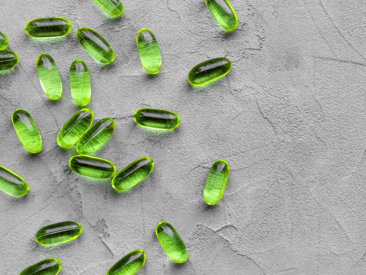 green soft gelatin transparent capsules laid out on a gray concrete background with copy space . The concept of pharmacology, homeopathy and medicine,peppermint candies, medicinal herbs