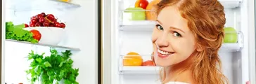 Happy woman standing at the open refrigerator with fruits