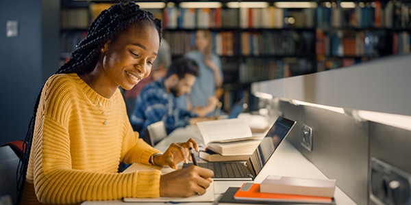 woman in yellow sweater working on a computer in a library area