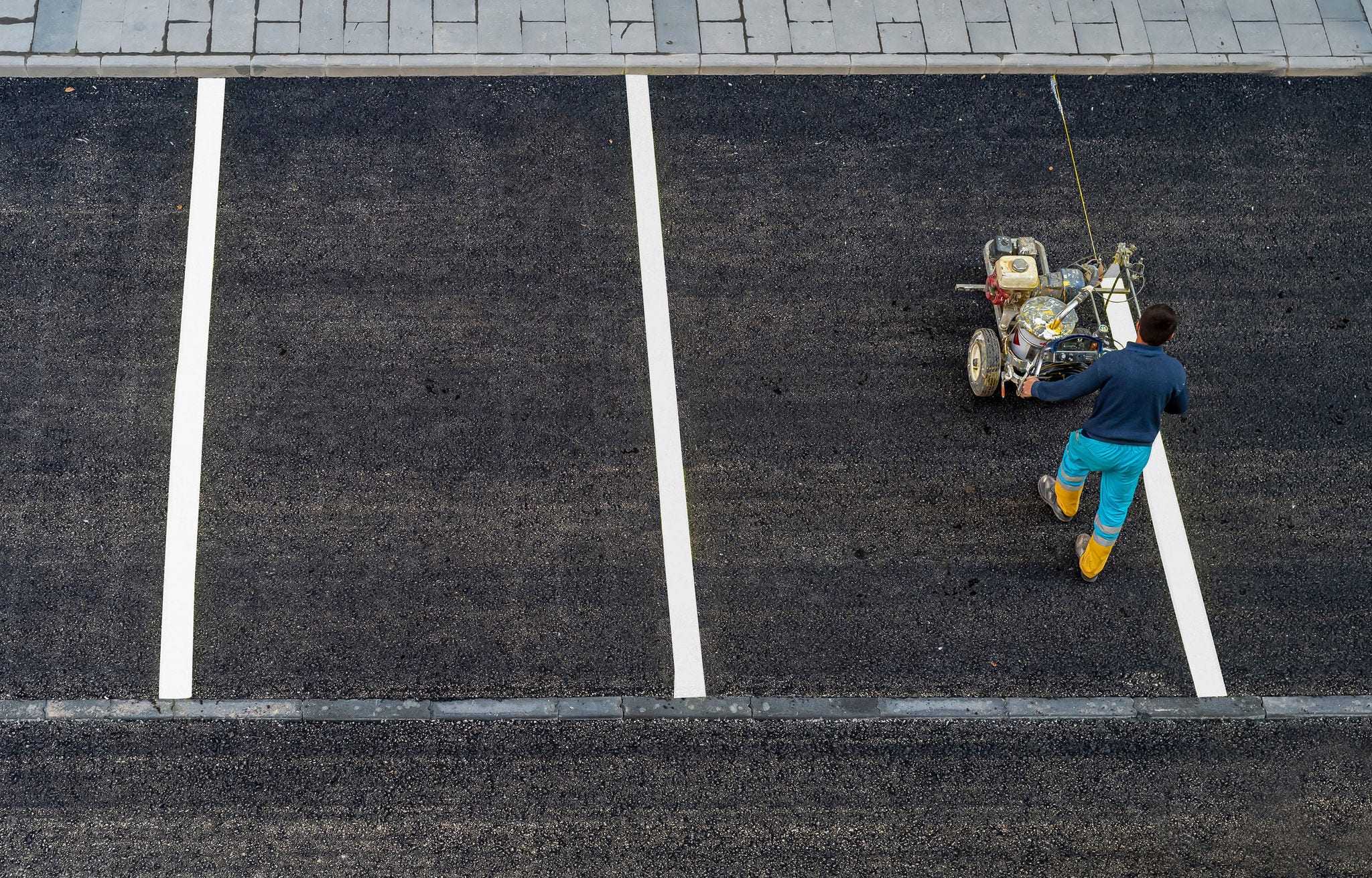 Worker paints a white line on an asphalt parking lot 