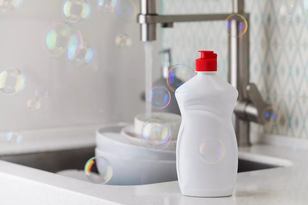 White dish soap bottle with soap bubbles and dishes in sink
