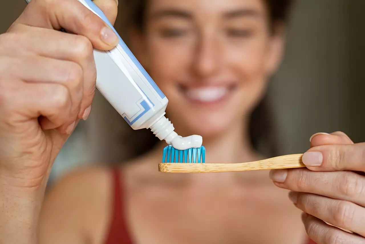Woman applying toothpaste on bamboo toothbrush 