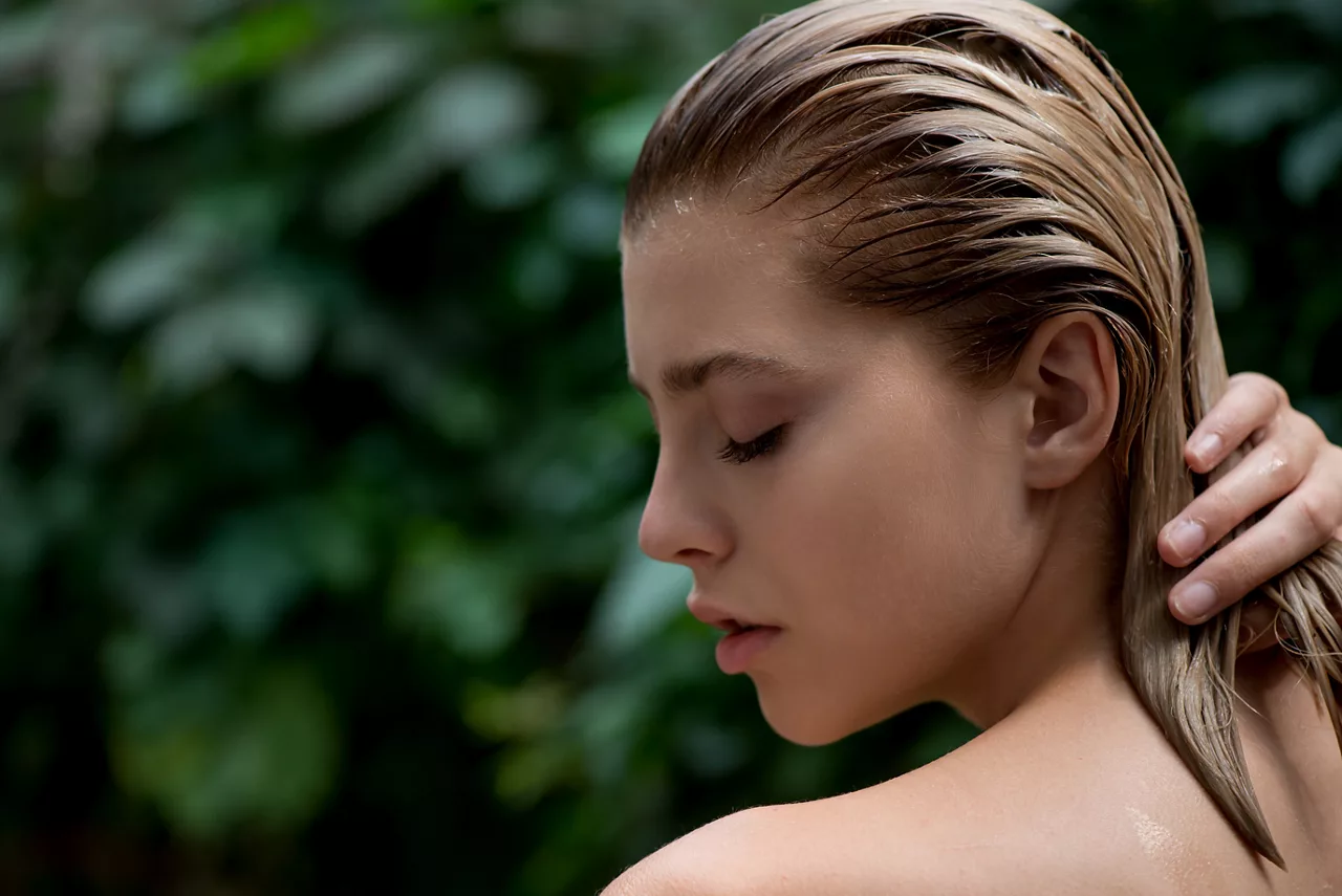 Beautiful young woman applies a balm, shampoo or conditioner to her damaged hair