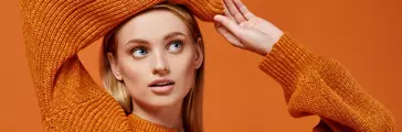 A woman in an orange sweater poses with her arms above her head 