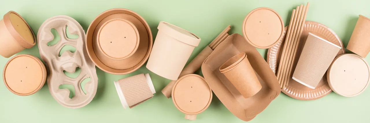 Paper utensils and disposable tableware, food containers and paper cups over green background