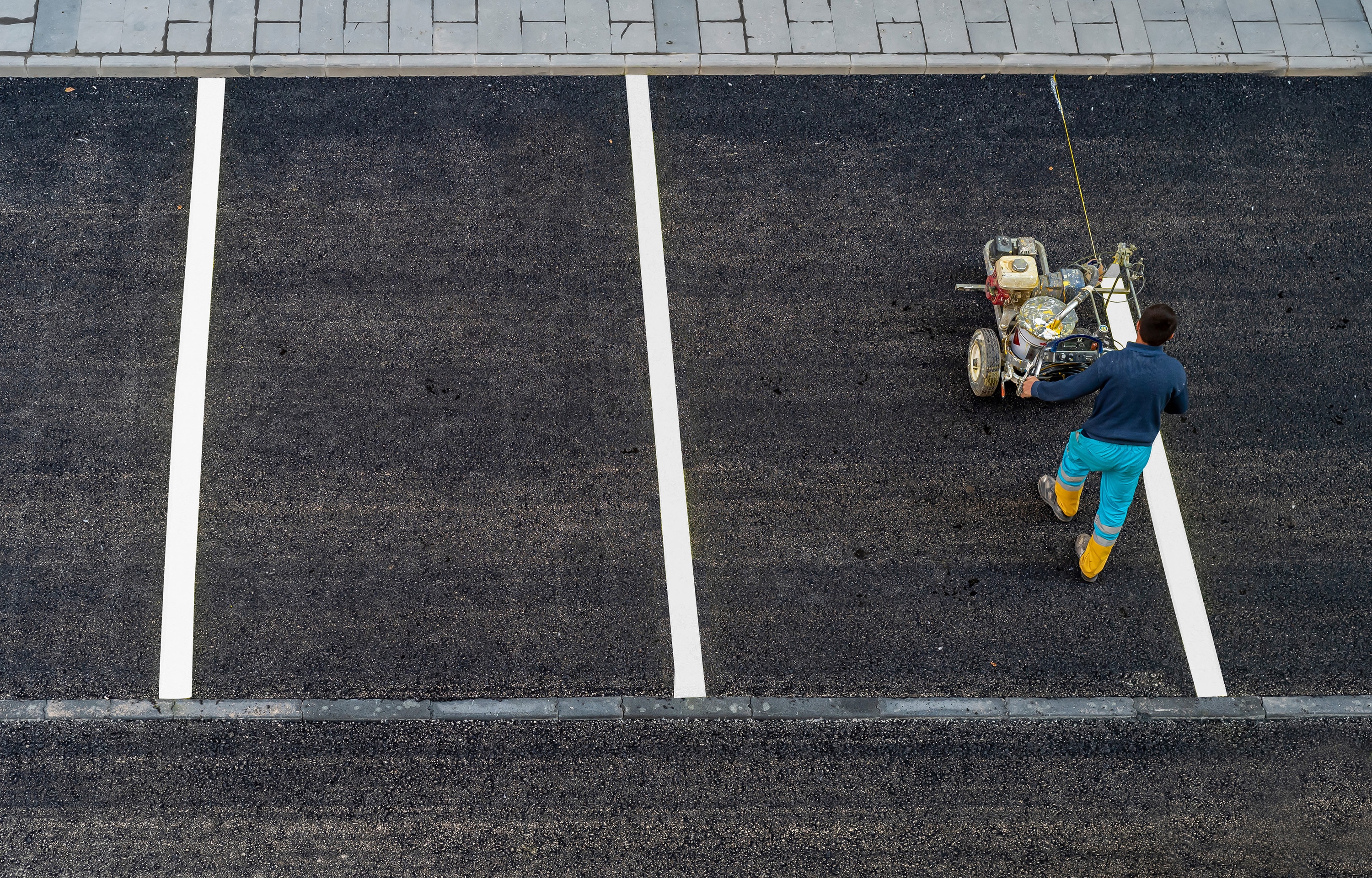 Worker paints a white line on an asphalt parking lot  