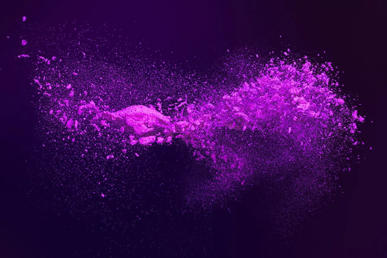 Dynamic burst of vibrant magenta and violet powder particles isolated against a dark background. for advertising, cosmetic effects, and abstract design overlay.